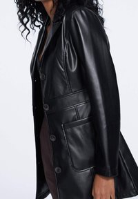 Abrigo de cuero negro con diseño entallado, botones abotonados simples, bolsillos laterales y un acabado suave, que acentúa una silueta elegante.