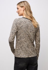 Pitkähihainen beige paita mustilla leopardikuvioilla, jossa on pyöreä kaula-aukko ja kiinteä siluetti. Suuri kangaslaatu, minimaalinen koristelu.