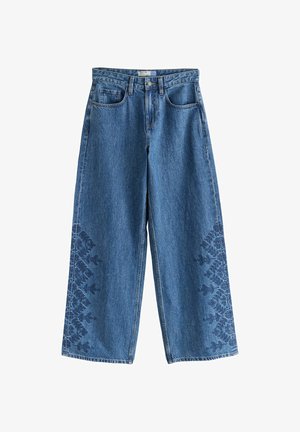 Modré džínsové nohavice so širokými nohavicami s kvetinovou výšivkou na spodnej vonkajšej časti nohavíc a klasickým päťvreckovým dizajnom.