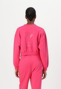 Fuchsia cropped sweatshirt with ribbed cuffs and hem, featuring embossed branding on the back. Paired with matching joggers.