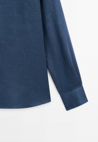 Dark blue button-up shirt with long sleeves, made of textured fabric; features a straight hemline and single cuff detail.
