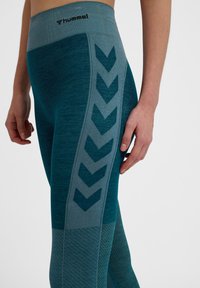 Leggings sportivi color teal con vita alta, caratterizzati da un motivo testurizzato e un design a zigzag in contrasto lungo il lato.
