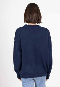 Un pull surdimensionné bleu marine en matière tricotée douce, avec un col rond et des poignets côtelés, vu de dos.