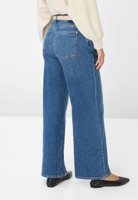 Jeans in denim blu a gamba larga con una finitura sbiadita, vita media e due tasche posteriori. Abbinati a delle ballerine nere e una maglietta chiara.