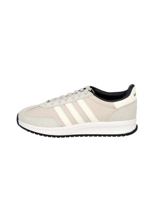Zapatilla Adidas beige y blanco roto con forro interior negro, cierre de cordones, tres franjas laterales y suela acolchada blanca con banda negra.