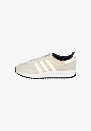 Zapatilla Adidas beige y blanco roto con forro interior negro, cierre de cordones, tres franjas laterales y suela acolchada blanca con banda negra.