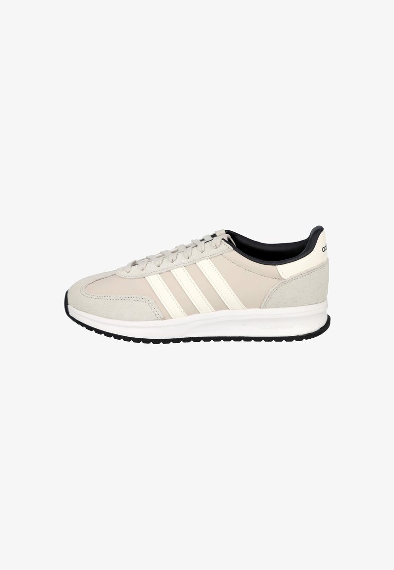 Zapatilla Adidas beige y blanco roto con forro interior negro, cierre de cordones, tres franjas laterales y suela acolchada blanca con banda negra.