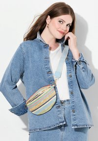 Bolso bandolera redondo de paja con rayas multicolores, acentos dorados y una correa ajustable de color azul claro. Se lleva con una chaqueta de mezclilla.