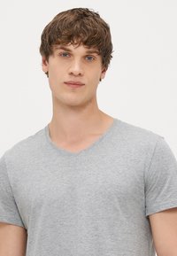 Γκρι μπλουζάκι με V λαιμόκοψη, κατασκευασμένο από βαμβάκι, με κοντά μανίκια και λεία υφή. Απλός σχεδιασμός, χωρίς σχέδια ή διακοσμητικά στοιχεία.