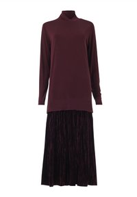 Langärmliges bordeauxfarbenes Rollkragenoberteil, kombiniert mit einem dunkelpurpurnen samtigen, gefalteten Maxirock vor einem weißen Hintergrund.