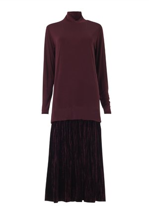 Top de cuello alto burdeos de manga larga combinado con una falda larga de terciopelo plisada en púrpura oscuro contra un fondo blanco.