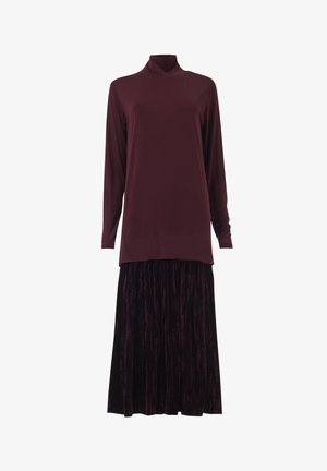 Top de cuello alto burdeos de manga larga combinado con una falda larga de terciopelo plisada en púrpura oscuro contra un fondo blanco.