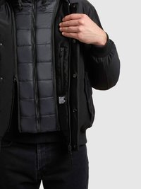 Czarna kurtka bomber z pikowanym, wyściełanym wnętrzem. Posiada zamki błyskawiczne i zapięcia na zatrzaski, ściągacze na rękawach oraz subtelną naszywkę z logo.