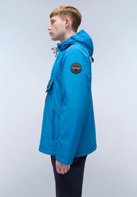 Giacca con cappuccio blu realizzata in tessuto impermeabile, con una tasca frontale, cordino regolabile sul cappuccio e un logo circolare sulla manica.