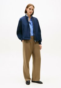 Marine bommerjack over een lichtblauw gestreept shirt, gecombineerd met beige wijde broek. Geweven materialen en een relaxed fit.