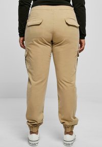 Beige cargo pants with side pockets, elastic ankle cuffs, and a stretchy waistband. Appears made of soft cotton blend material.