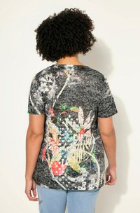 T-shirt noir avec un design floral multicolore au dos ; manches courtes, col rond et tissu texturé.