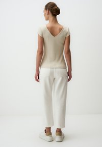 Top beige a coste con scollo a V e maniche corte, abbinato a pantaloni bianchi a vita alta. Calzature sono sneakers bianche con dettagli color cammello.