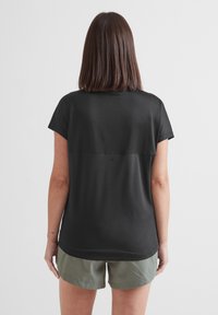 Black short-sleeve top featuring a relaxed fit with a smooth texture and a seam across the back. Paired with olive-green shorts.