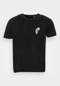 Svart t-shirt med avslappnad passform, med en turkos handgrafik som håller en rosa cirkel på vänster bröstarea, tillverkad av mjuk tyg.