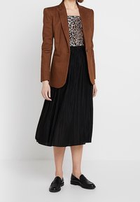 Brown tailored blazer over a leopard print top, paired with a black pleated midi skirt and black loafers. Textured fabric and structured design.