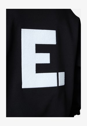 Black sweatshirt featuring a large, white textured capital "E." The letter has a soft, fuzzy surface contrasted against the smooth fabric.