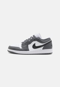 Sive i bijele kožne niske tenisice s crnim detaljima, perforiranim prednjim dijelom i bijelim gumenim potplatom. Uključuje klasični Nike Swoosh logotip.
