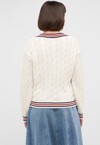 Kremowy sweter w splot pętelkowy z prążkowanym dołem, zdobiony czerwono-białymi i niebieskimi paskami. Długie rękawy i teksturowany wzór na całej powierzchni.
