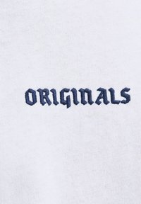 Balta auduma ar tumši zilu izšūtu tekstu, kurā rakstīts "ORIGINALS" iedvesmojošā, stilizētā fontā. Auduma virsma ir gluda un nedaudz teksturēta.