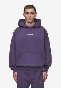 Felpa di cotone viola con tasca frontale e cappuccio con cordino. Presenta il logo "PEGAADOR" in bianco sul petto. Tessuto morbido, vestibilità comoda.