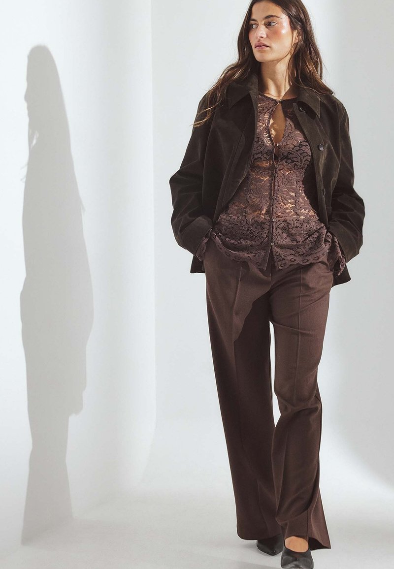 Brown corduroy jacket over a brown lace top, paired with brown wide-leg pants. The outfit features a light sheen and textured details.