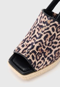 Πλατφόρμα σανδάλι με επάνω μέρος από ύφασμα με λεοπάρ μοτίβο, μαύρο σχέδιο ανοιχτού δαχτύλου και σόλα τυλιγμένη με σχοινί τζούτας. Διαθέτει γυαλιστερές λεπτομέρειες πάνω στο μοτίβο.