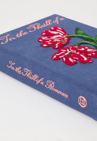 Copertina blu con fiori ricamati rossi e bianchi e testo arancione in corsivo che legge "Nel brivido di un amore."