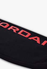 Μαύρη υφασμάτινη κορδέλα κεφαλής με εμφανή κόκκινα γράμματα "JORDAN". Μαλακή υφή, κυρτό σχήμα, σχεδιασμένη για αθλητική χρήση.