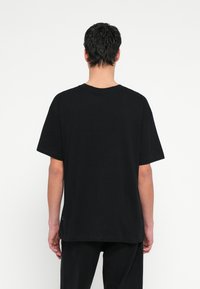 Μαύρο βαμβακερό μπλουζάκι με άνετη εφαρμογή, κοντά μανίκια και στρογγυλή λαιμόκοψη. Απλός σχεδιασμός, χωρίς σχέδια ή διακοσμήσεις.