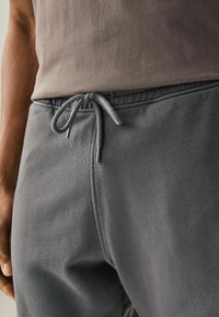 Graue Sweatpants mit einer strukturierten Oberfläche verfügen über einen Kordelzugbund, silberne Metallspitzen am Kordelzug und einen lockeren Schnitt.
