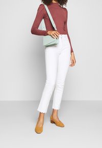 Haut ajusté couleur bordeaux, jean blanc slim, chaussures jaunes à talons carrés tressées, et sac bandoulière vert clair au design simple avec une sangle réglable.