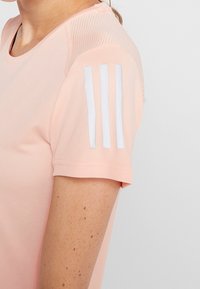 Světle růžové atletické tričko s krátkými rukávy, texturední látka, síťovina na ramenou a tři bílé pruhy na rukávu.