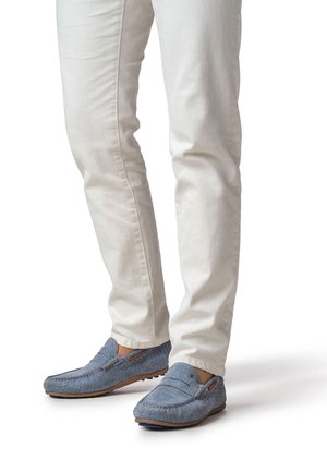 Mocasines de cuero azul claro con acabado texturizado y detalles elásticos laterales, combinados con vaqueros blancos de corte ajustado.