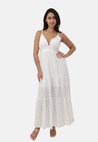 Witte maxi jurk met een diepe V-hals, verstelbare spaghetti banden, gelaagd ontwerp en oogjes borduursel patroon. Soepele stof textuur.