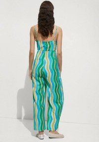 Tuta a righe verde e blu con spalline sottili, design a gamba larga, caratterizzata da motivi ondulati e un tessuto leggero e traspirante.