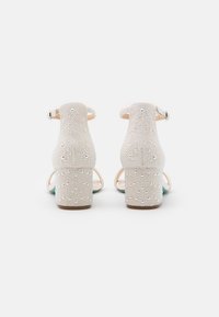 Sandali con tacco bianchi caratterizzati da una superficie testurizzata decorata con numerosi piccoli chiodini iridescenti, cinturino alla caviglia e design con tacco a blocco.