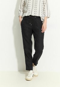 Pantaloni jogger neri in lino con vita regolabile, tasche laterali e vestibilità rilassata, abbinati a una blusa bianca a righe e scarpe da ginnastica bianche.