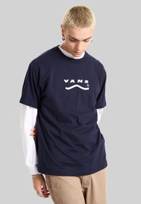 Camiseta de algodón azul marino con un logo blanco de "VANS" con un acento curvado. Mangas cortas y un diseño clásico de cuello redondo.