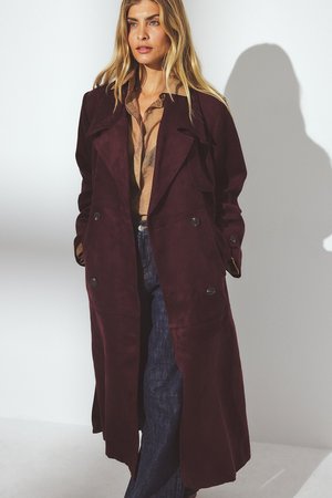 Lång bordeauxfärgad mockajacka med dubbelknäppt design, stora knappar och krage; lagd över en beige topp och denimjeans.
