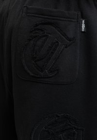 Black sweatpants featuring a textured and embroidered logo on the back pocket and a fabric tag labeled "WASTED." Soft cotton material.