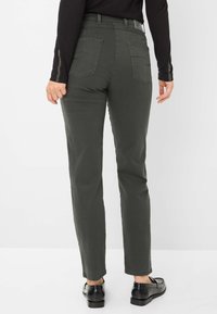Pantaloni slim fit a vita alta di colore verde scuro, con tasche posteriori e una texture liscia. Indossati con scarpe nere. Inquadratura dal retro, sfondo neutro.