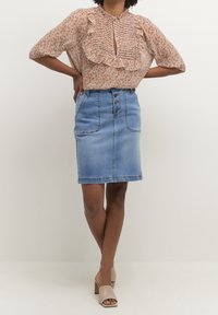 Květinová halenka s volánky a detailním průstřihem, doplněná modrou džínovou sukní s předním zapínáním na knoflíky a dvěma bočními kapsami.