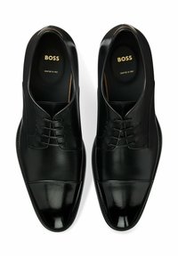 Black leather dress shoes featuring a smooth texture, lace-up closure, rounded toe, and glossy cap toe detail. Logo displayed on insole.