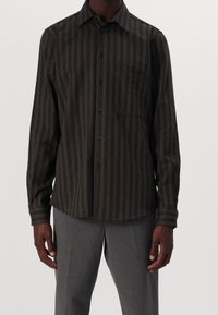 Ciemnozielona koszula z długim rękawem zapinana na guziki, z pionowymi paskami, kieszenią na piersi i czarnymi guzikami. Miękka tekstura, luźny krój.